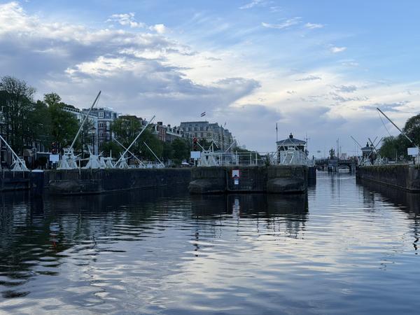 This photo captures a serene view of the Amstel river in Centrum, Amsterdam, showcasing the intricate canal lock system under a partly cloudy sky